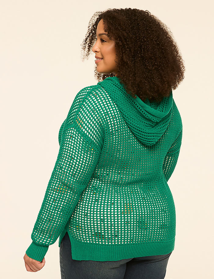 A woman in a green hooded sweater stands against a plain, light-colored background.
