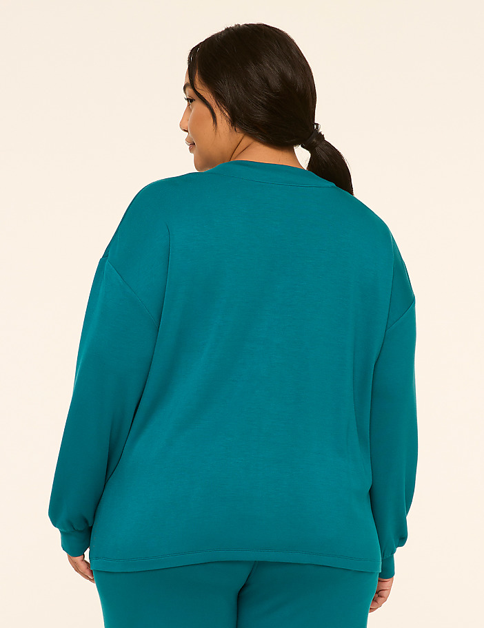 A woman in a teal sweatshirt and pants stands against a plain, light-colored background.
