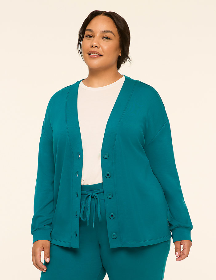 A woman in a teal cardigan and matching pants stands against a plain, light-colored background.