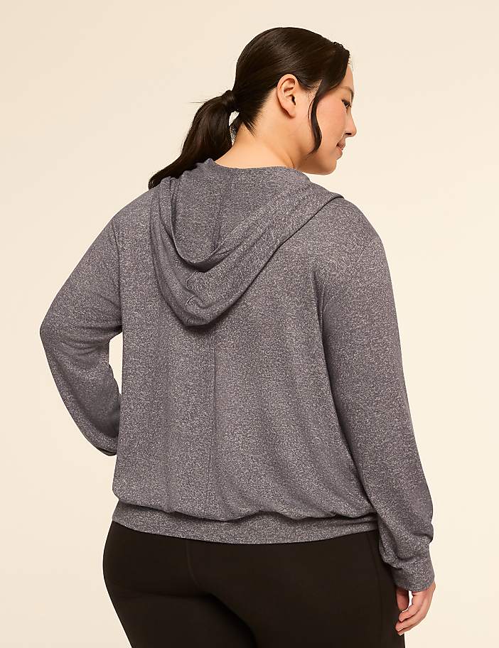 A woman in a grey hoodie and black leggings stands against a plain, light-colored background.