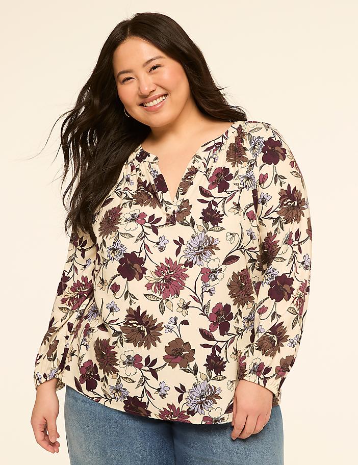 A smiling woman in a floral blouse stands against a plain, light-colored background.