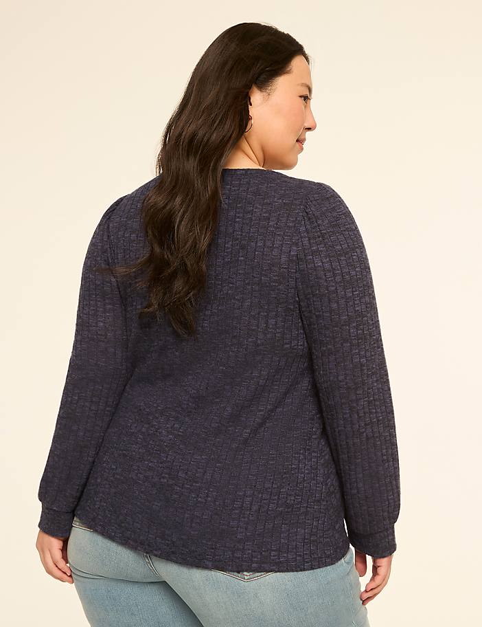 A woman in a dark blue textured top and light blue jeans stands against a plain, light-colored background.