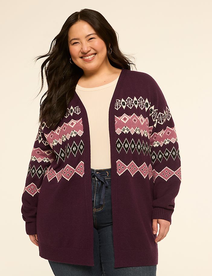 A smiling woman in a patterned cardigan stands against a plain, light-colored background.