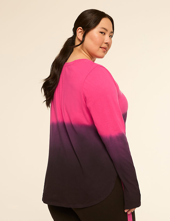 A woman in a pink and purple tie-dye shirt stands against a plain, light-colored background.