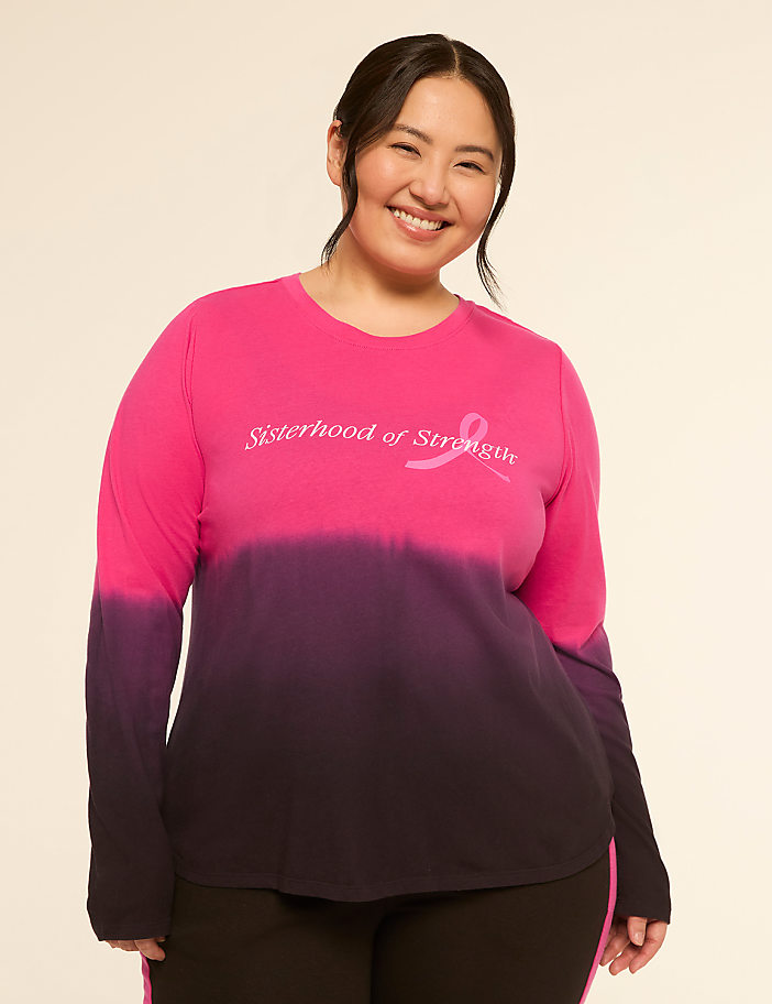 A smiling woman in a pink and purple ombre long-sleeved shirt stands against a plain, light background.