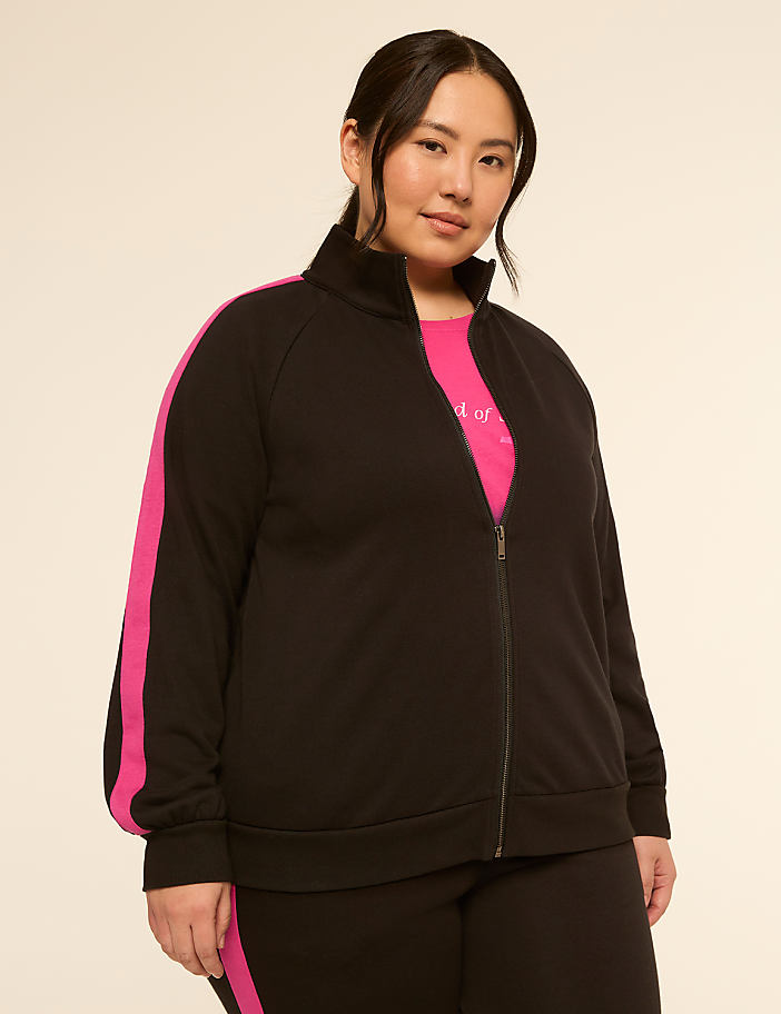 A woman in a black zip-up jacket with pink stripes stands against a plain, light-colored background.