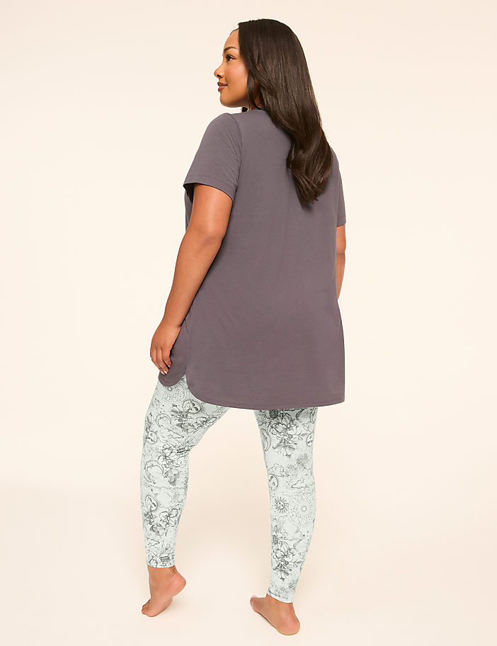 A woman in a grey tunic and patterned leggings stands with her back to the viewer against a plain, light background.