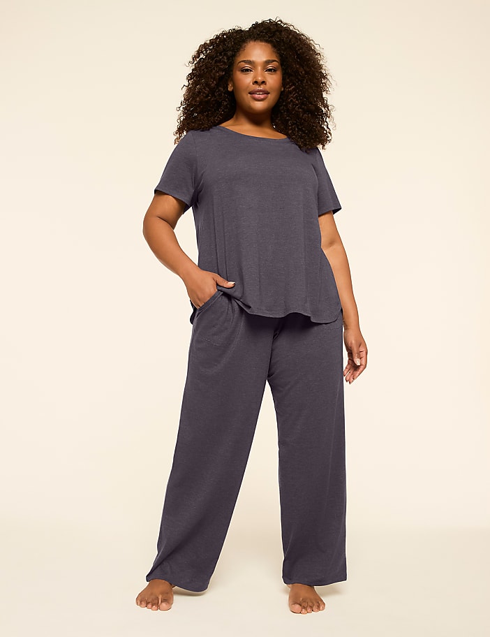 A woman in a navy blue pajama set stands against a plain, light beige background.