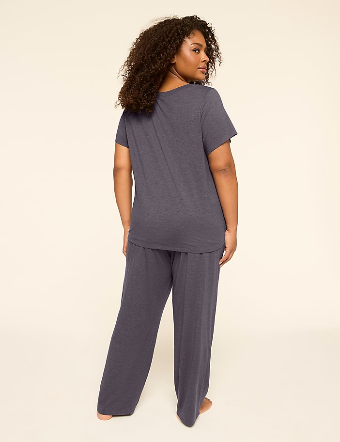 A woman in dark blue pajamas stands facing away from the camera against a plain, light-colored background.