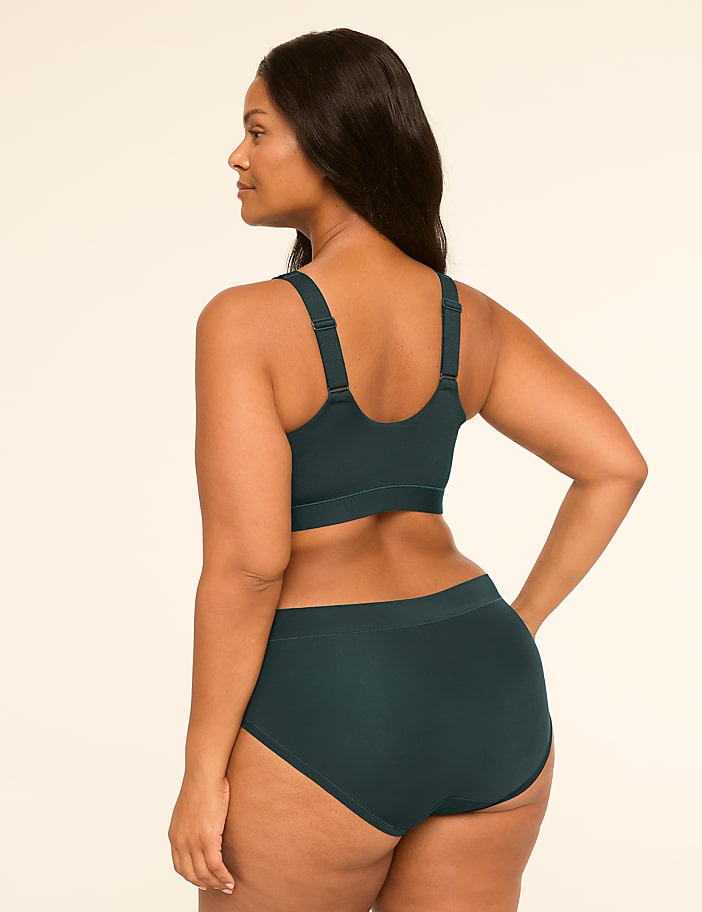 A woman in dark green lingerie stands against a plain, light background.