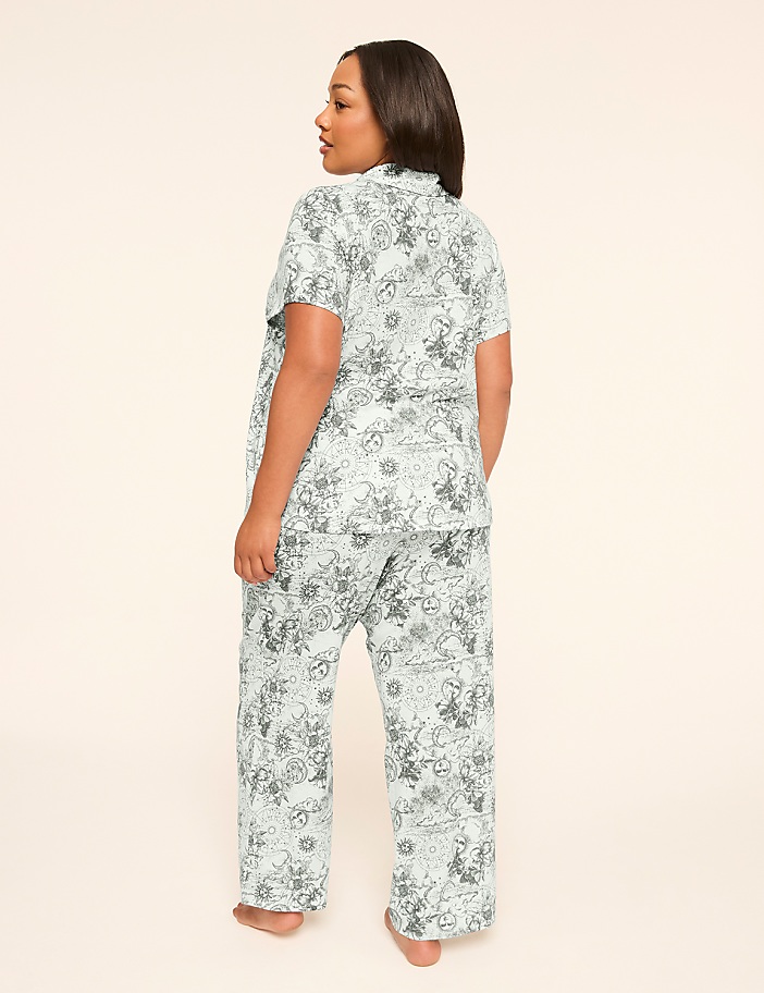 A woman in a light blue patterned pajama set stands with her back to the viewer against a plain, light background.