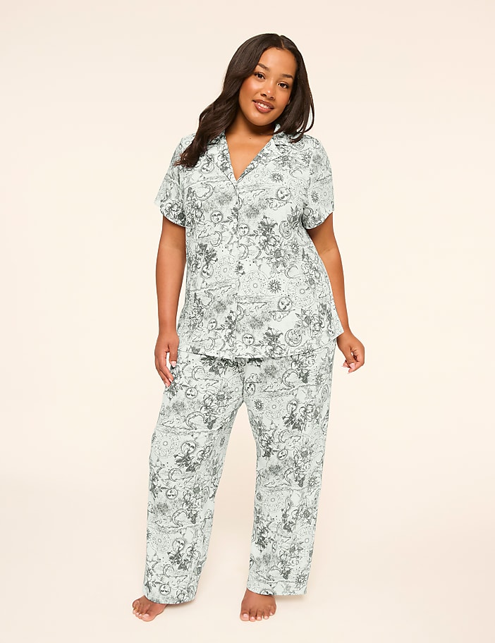 A woman stands in a light blue pajama set with a cartoon print against a plain, light background.