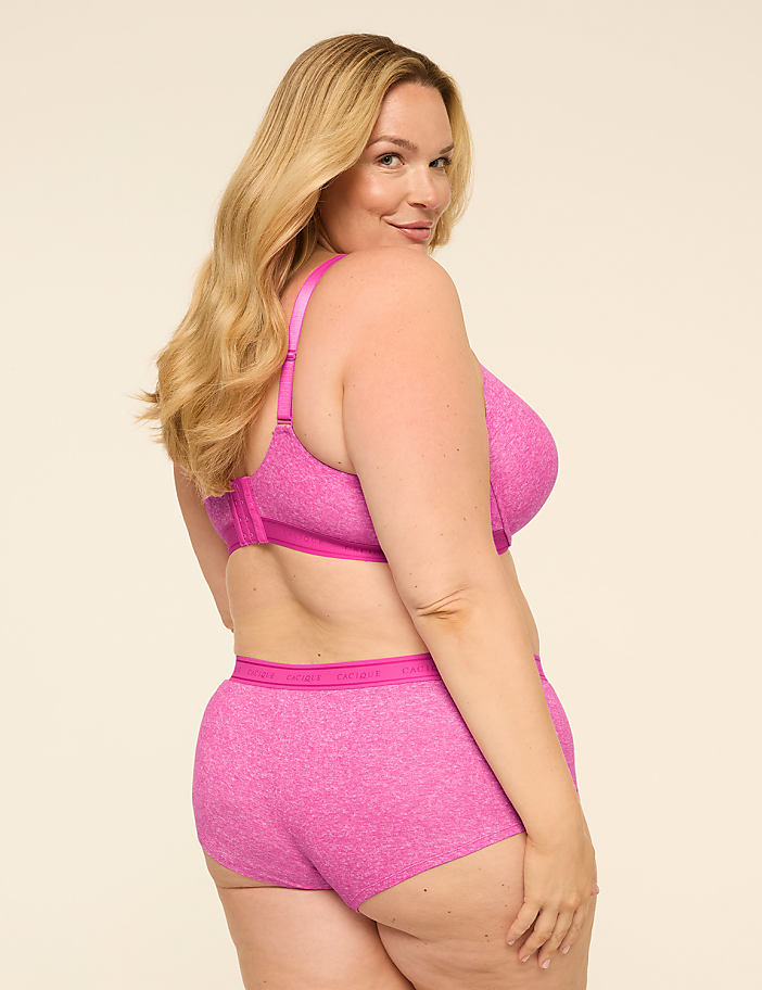 A woman with blonde hair and a fuller figure poses in pink lingerie against a plain, light-colored background.
