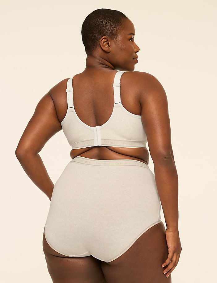 A woman in a beige bra and high-waisted briefs stands against a plain, light-colored background.