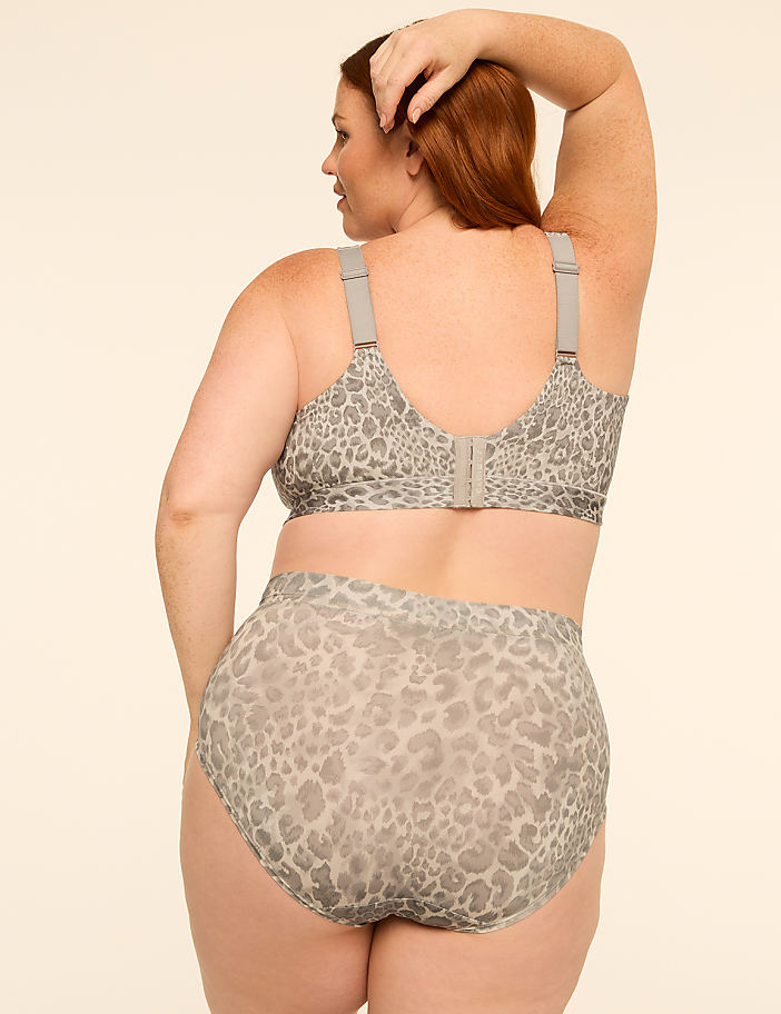 A woman with red hair is shown from behind, wearing a leopard-print bra and high-waisted underwear against a plain, light-colored background.