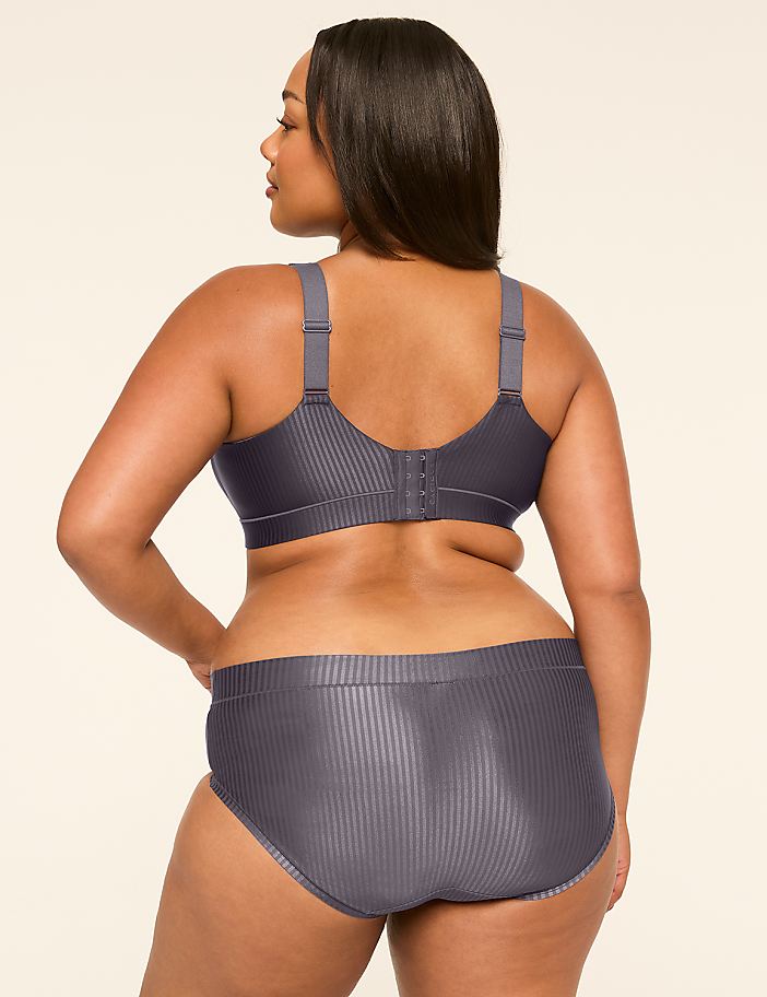 A woman in a grey ribbed bra and underwear stands with her back to the camera against a plain, light-colored background.