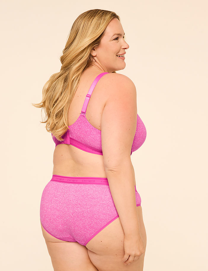 A woman in a pink bra and underwear stands against a plain, light-colored background.