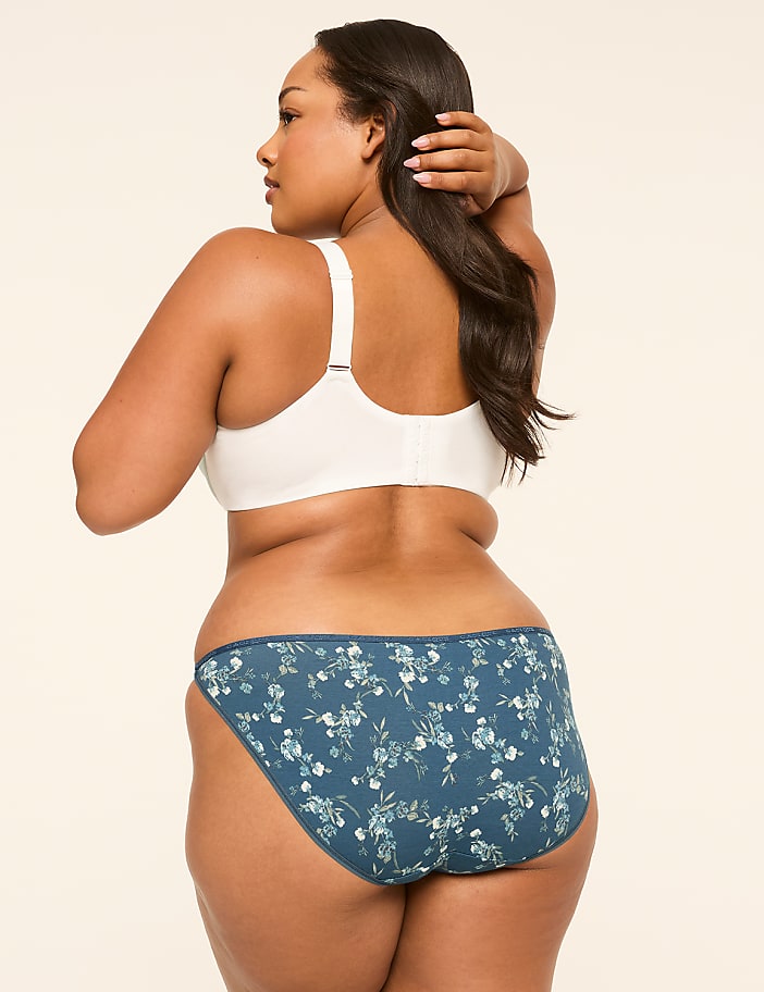A woman in a white bra and floral underwear stands against a plain, light-colored background.