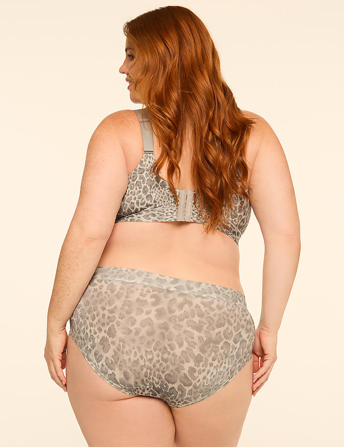 A woman with red hair, wearing a leopard print bra and underwear, stands against a plain, light-colored background.