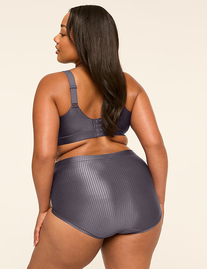 A woman in a grey ribbed bra and high-waisted briefs stands against a plain, light-colored background.