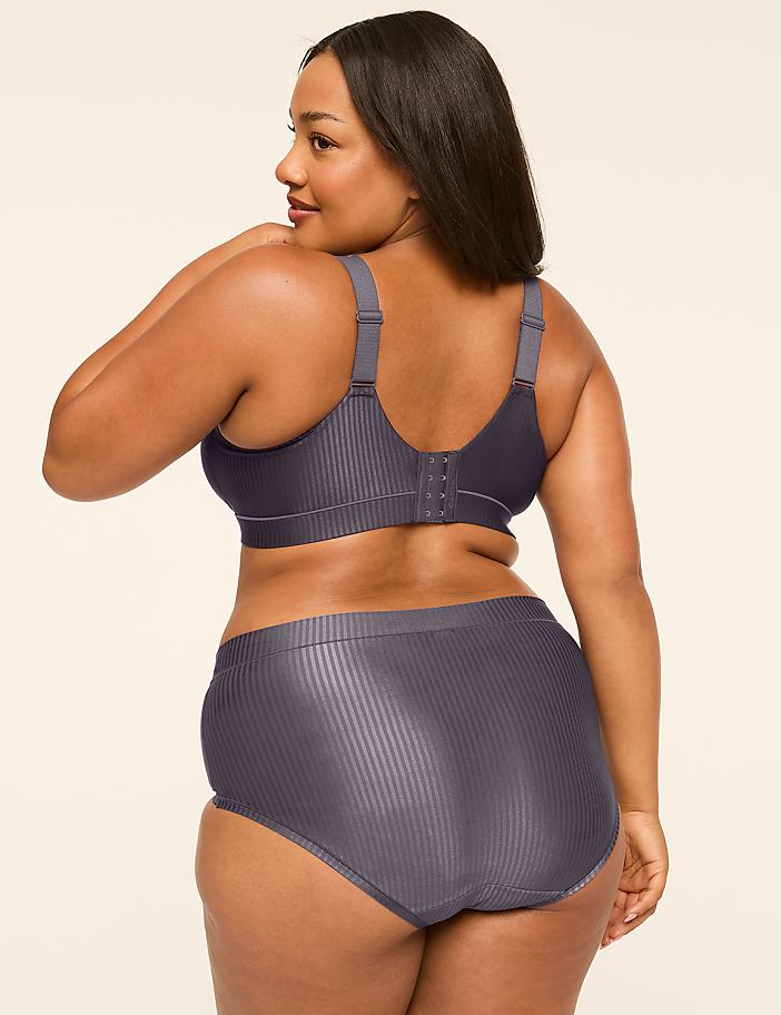 A woman in a grey bra and underwear stands against a plain, light-colored background.