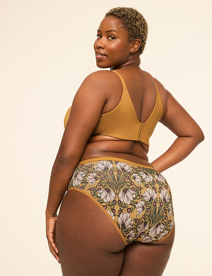 A woman in a mustard-colored bra and floral-patterned underwear poses against a plain, light-colored background.