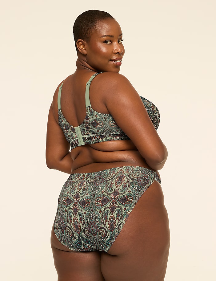 A woman with dark skin and short hair, wearing a patterned green bra and matching underwear, poses against a plain, light-colored background.