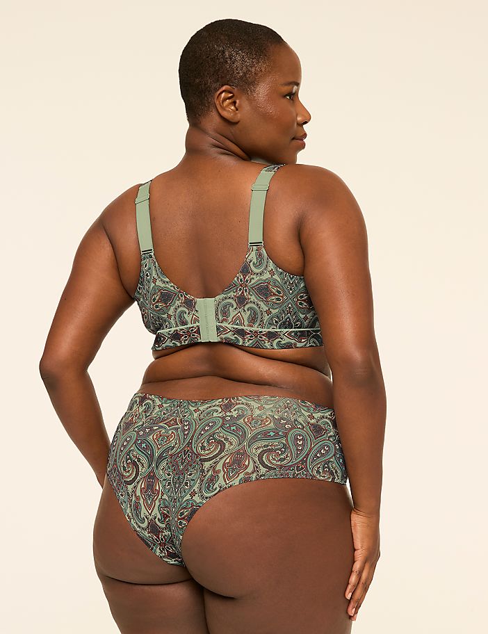 A woman with dark skin and short hair, wearing a green paisley-patterned bra and underwear, stands against a plain, light-colored background.
