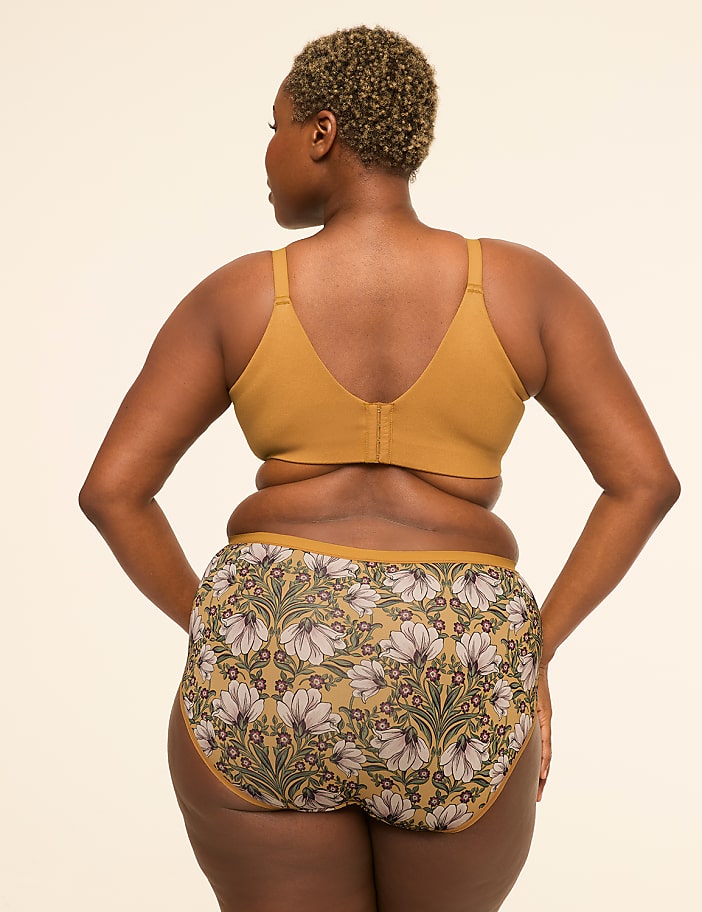 A woman in a mustard-colored bra and floral-patterned underwear stands against a plain, light-colored background.