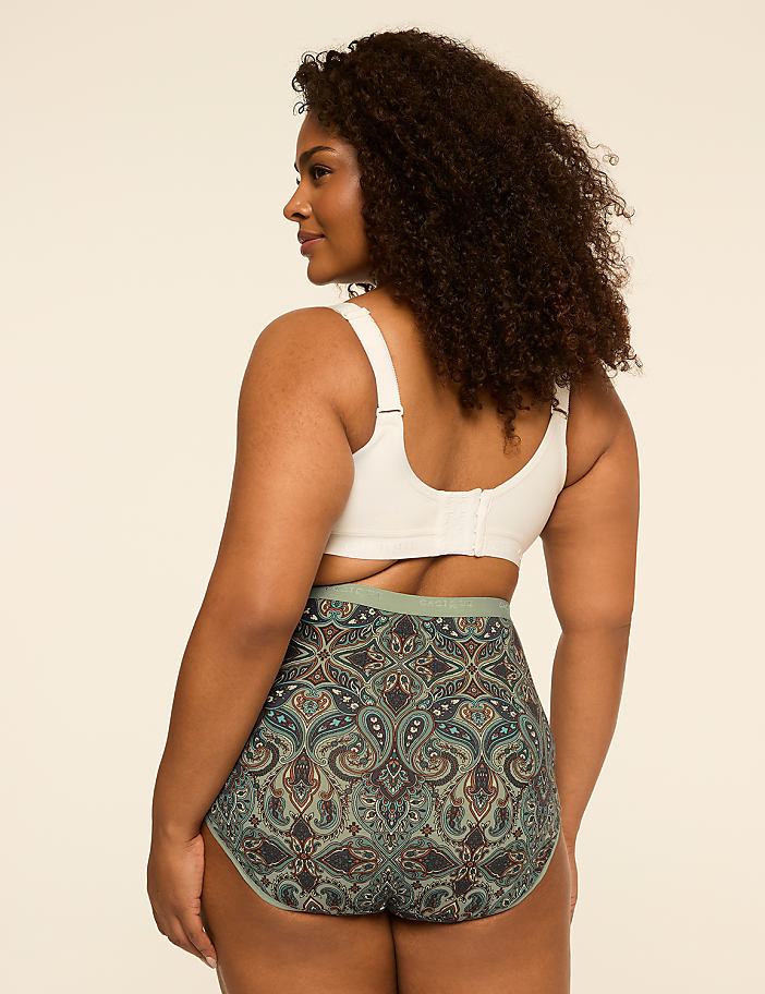 A woman in a white bra and patterned underwear stands against a plain, light-colored background.