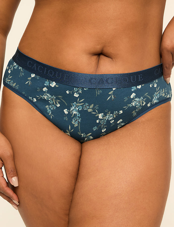 A close-up of a woman's lower torso wearing teal floral print underwear with a navy waistband, set against a plain, light background.