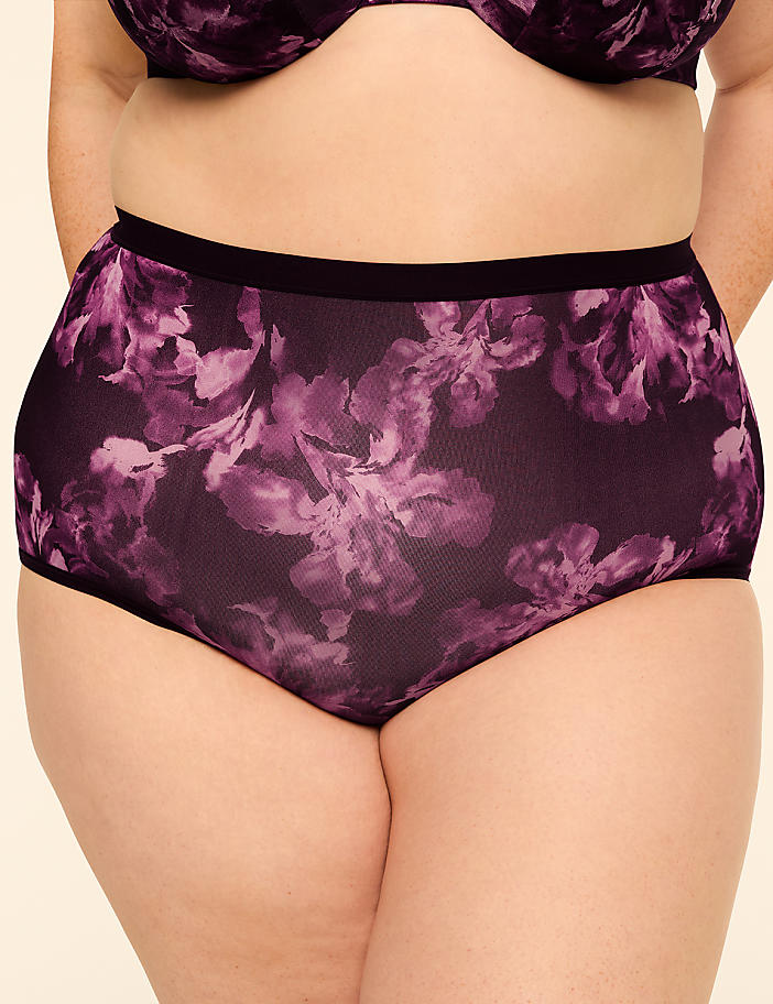 A person wears high-waisted purple floral underwear in the foreground, with a plain beige background.