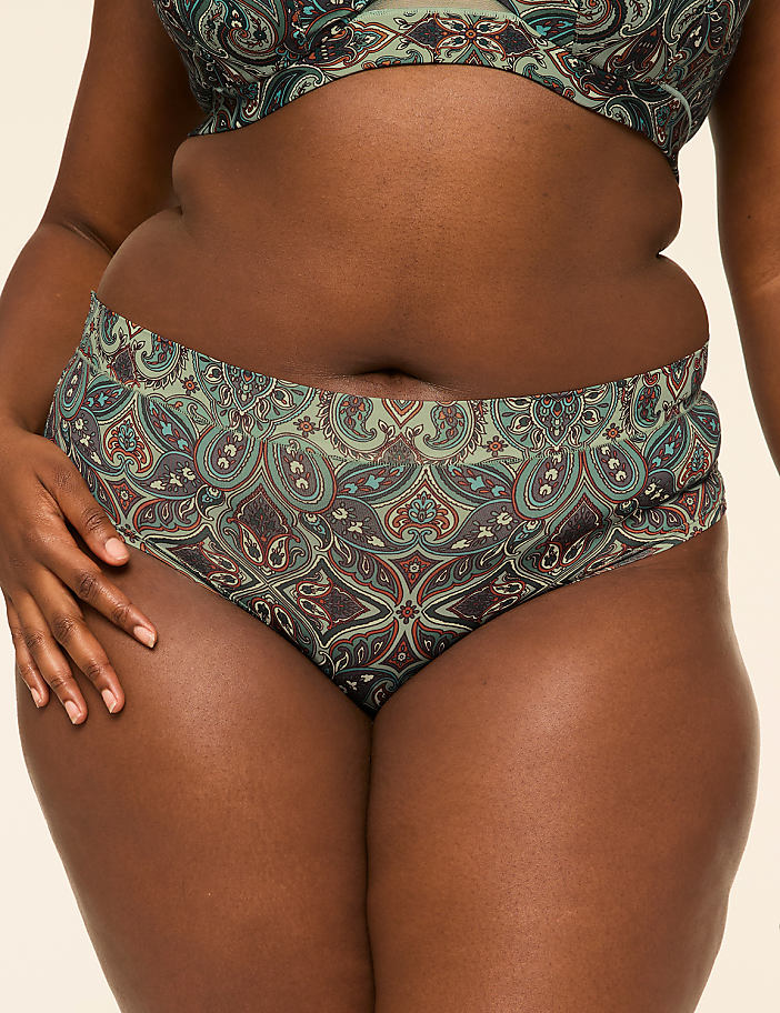A person in patterned swimwear stands against a plain, light-colored background.