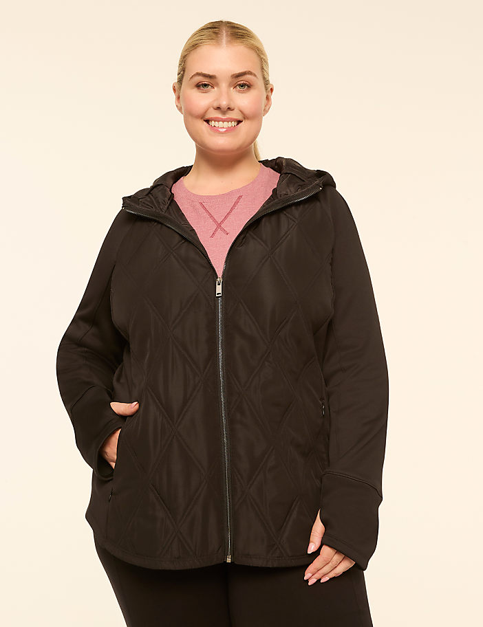 A smiling woman in a black quilted jacket stands against a plain, light-colored background.