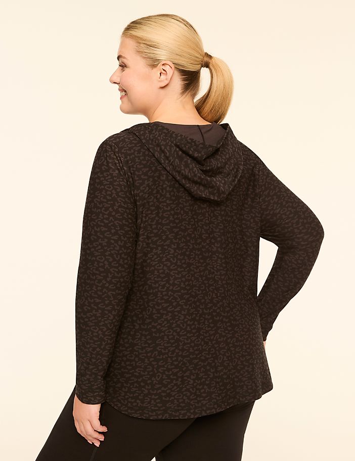 A woman in a patterned hoodie and leggings stands against a plain, light-colored background.