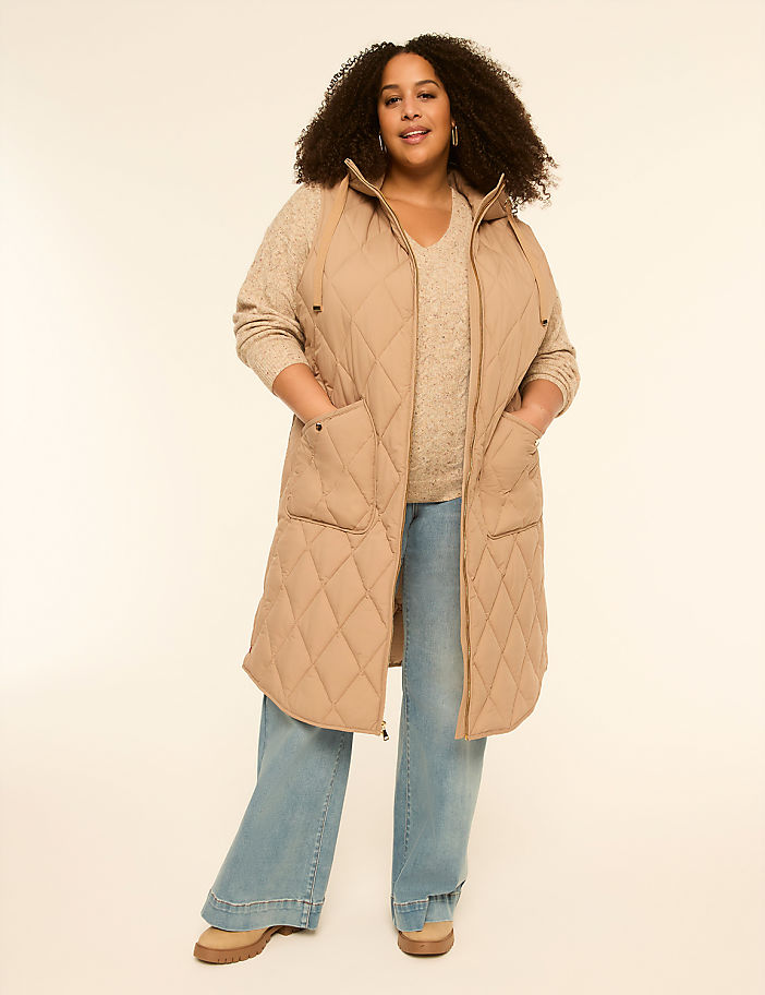 A woman in a quilted vest and wide-leg jeans stands against a plain, light-colored background.