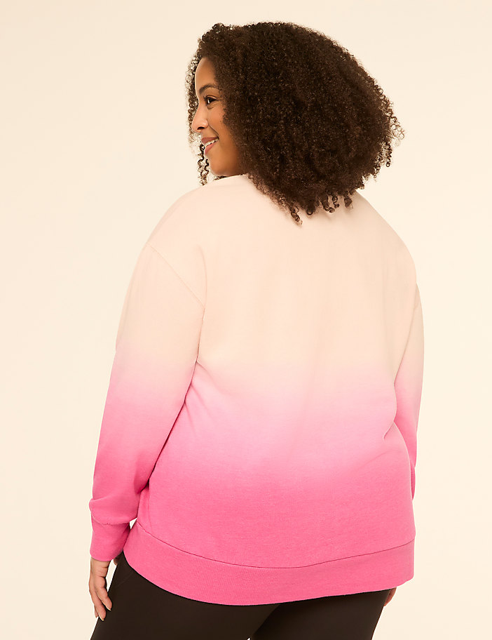 A woman in a pink and cream ombre sweatshirt stands against a plain, light-colored background.