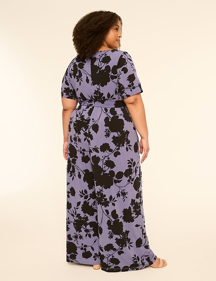 A woman in a floral jumpsuit stands against a plain, light-colored background.