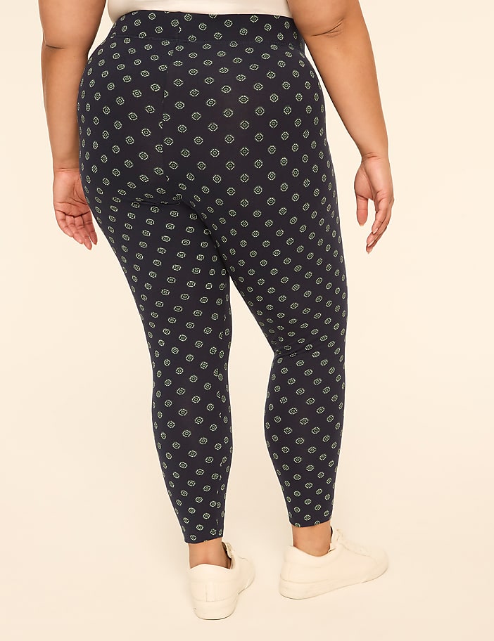 A person wearing patterned leggings and white sneakers stands against a plain, light-colored background.