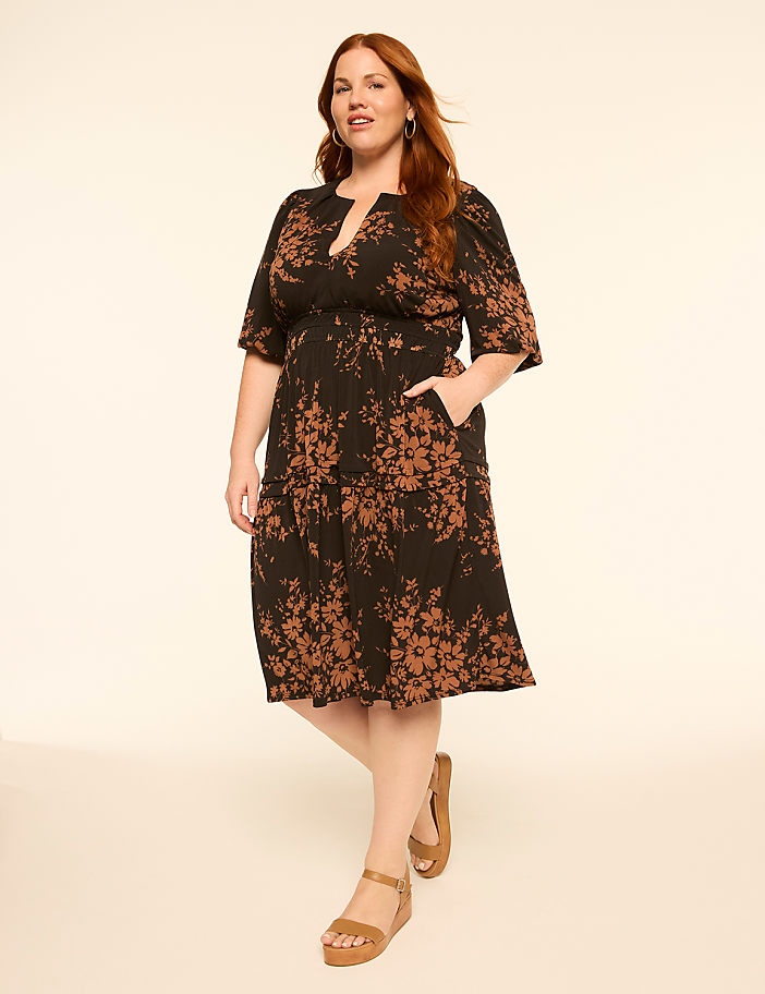 A woman in a floral print dress stands against a plain, light-colored background.