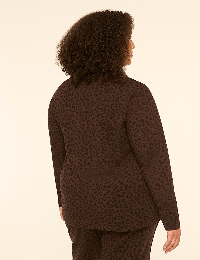 A woman with dark, curly hair stands with her back to the viewer, wearing a brown leopard-print blazer and pants against a plain, light-colored background.