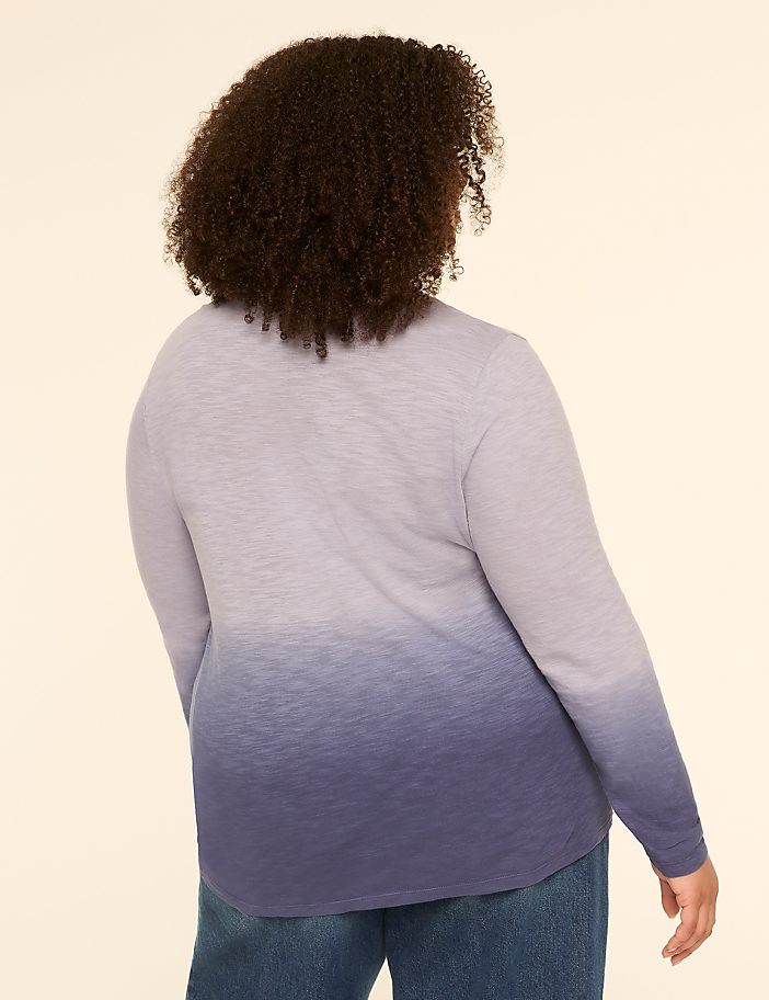 A woman with curly brown hair, seen from the back, wears a long-sleeved shirt with a purple to blue ombre gradient and blue jeans against a plain beige background.