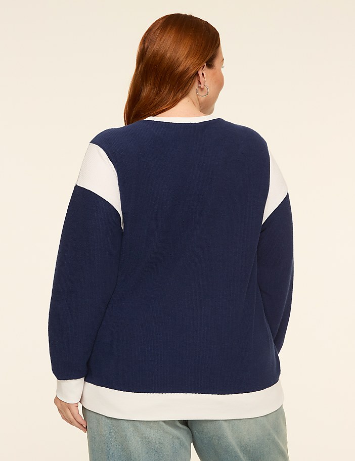 A woman with red hair wearing a navy and white sweatshirt stands against a plain, light-colored background.