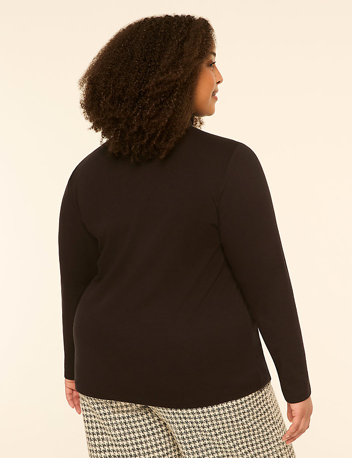 A woman with curly hair, seen from the back, wears a black long-sleeved shirt and patterned pants against a plain, light-colored background.