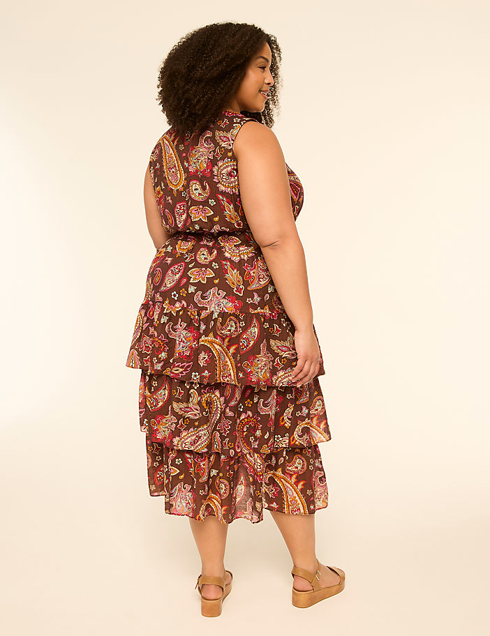 A woman in a paisley-print tiered dress stands against a plain, light-colored background.