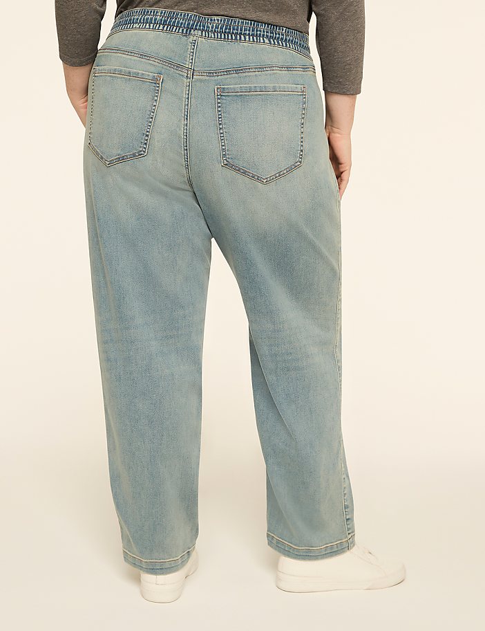 A person wearing light-wash denim jeans with a grey waistband stands against a plain, light-colored background.