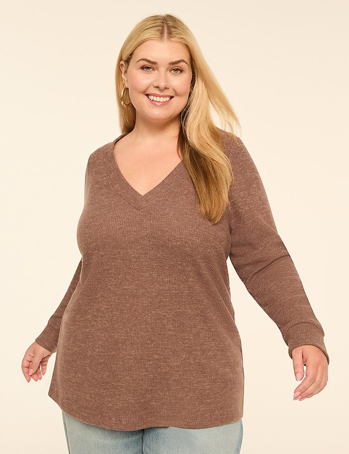 A smiling woman with blonde hair and a v-neck sweater stands against a plain, light-colored background.