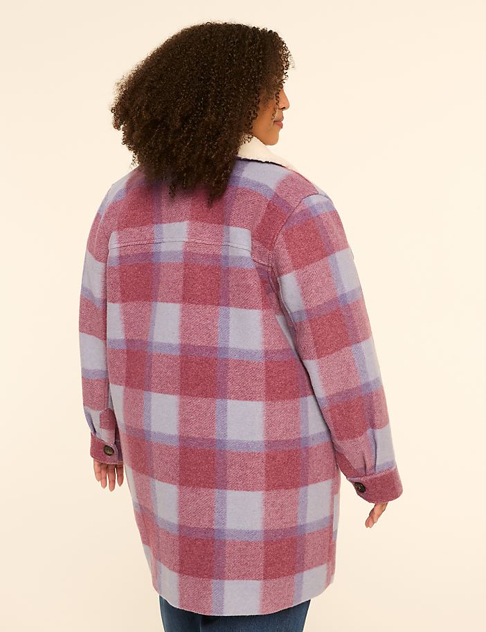 A woman in a pink and purple plaid jacket stands against a plain beige background.