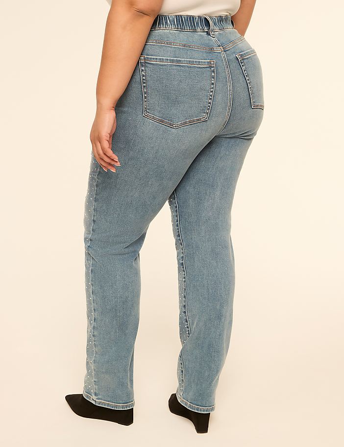A person wearing light blue jeans with embellished side seams stands against a plain, light-colored background.