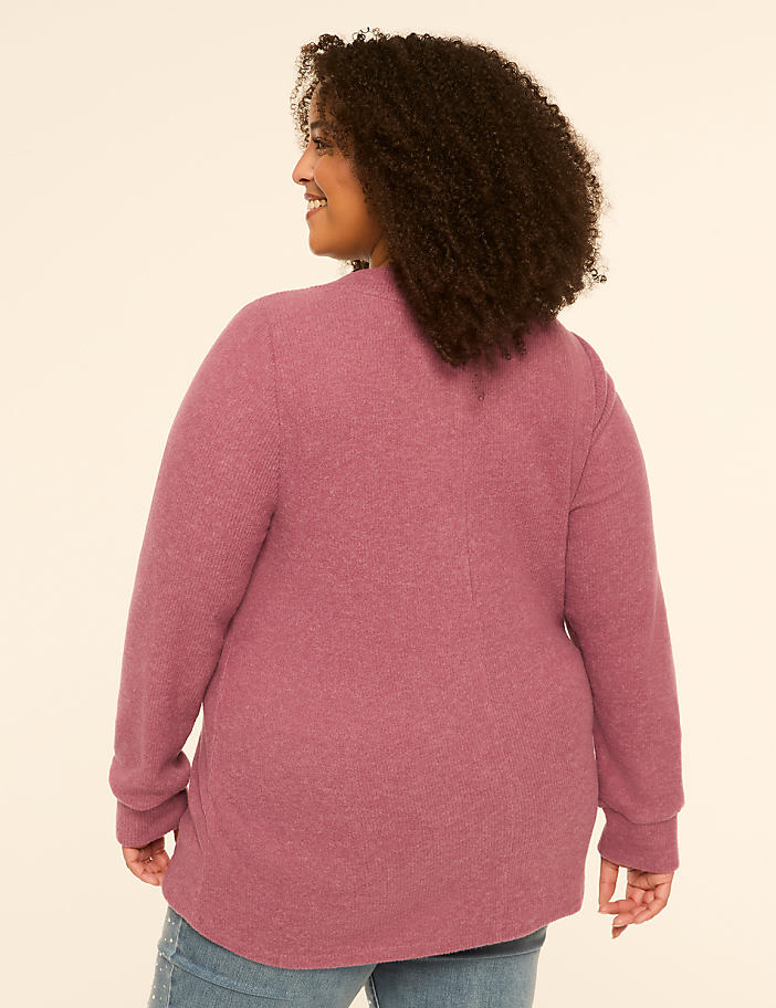 A woman in a mauve cardigan and jeans stands against a plain, light-colored background.